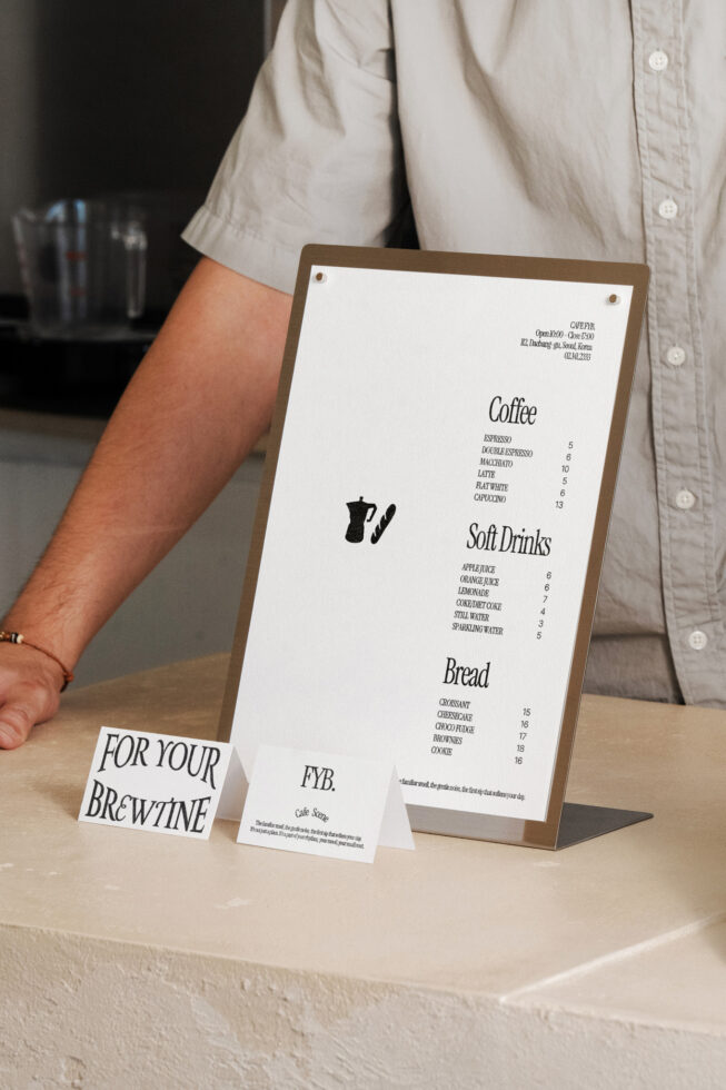 Person holding wooden menu board displaying coffee, soft drinks, bread pricing
