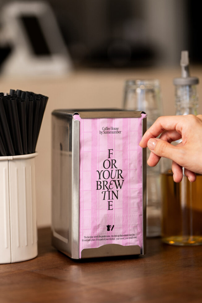 Pink gingham napkin box dispenser labeled For Your Brewtine surrounded by cafe supplies