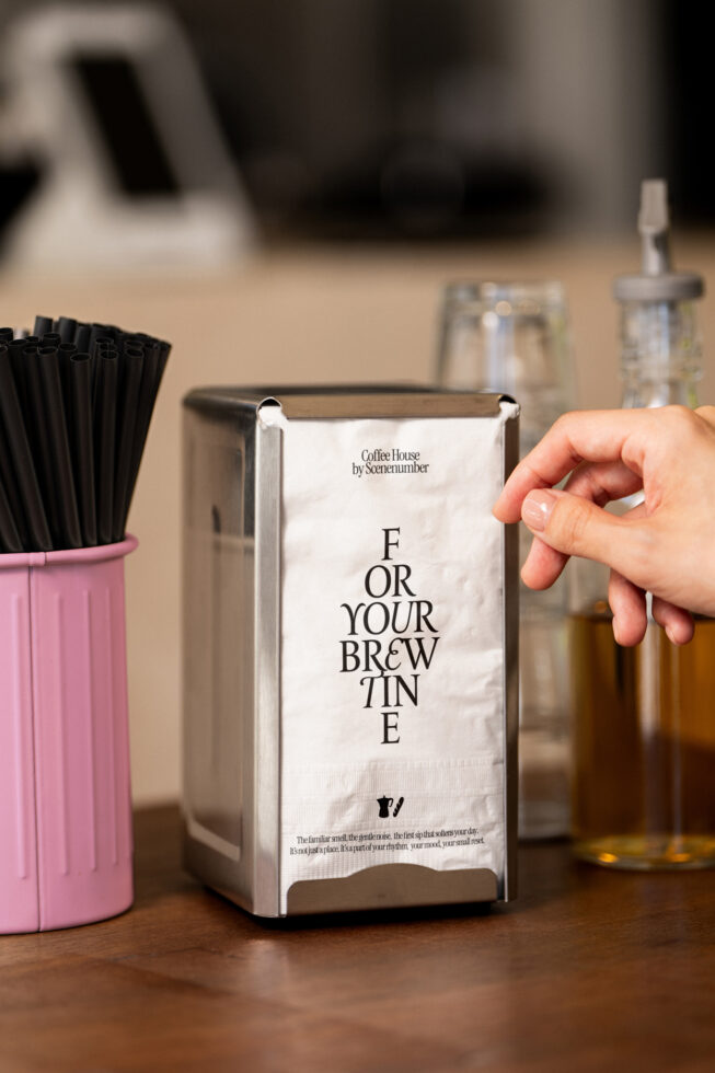 Hand holding napkin dispenser box with For Your Brewtine typography on counter
