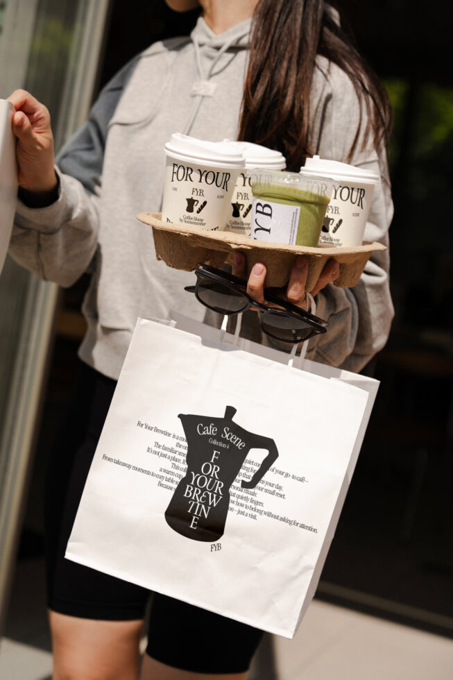 Hands holding white paper bag with coffee cups in cardboard carrier
