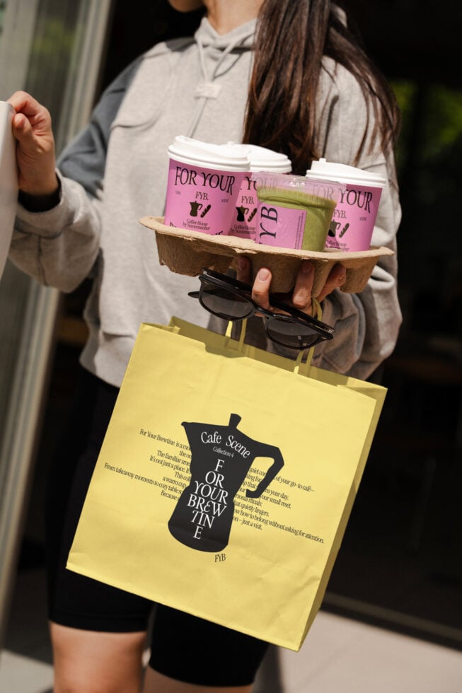 Woman holding yellow shopping bag with pink coffee cups in cardboard carrier, sunglasses visible