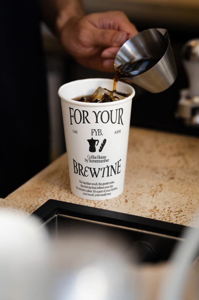 Barista pouring milk into coffee cup from metal jug, dark wood surface background