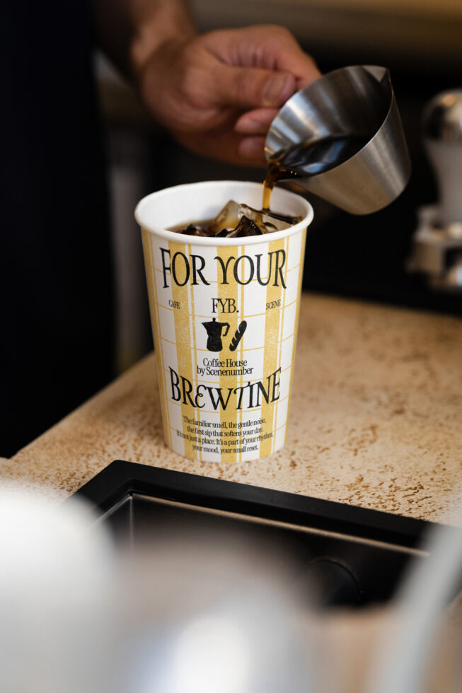 Barista pouring espresso into branded coffee cup with gold stripe design