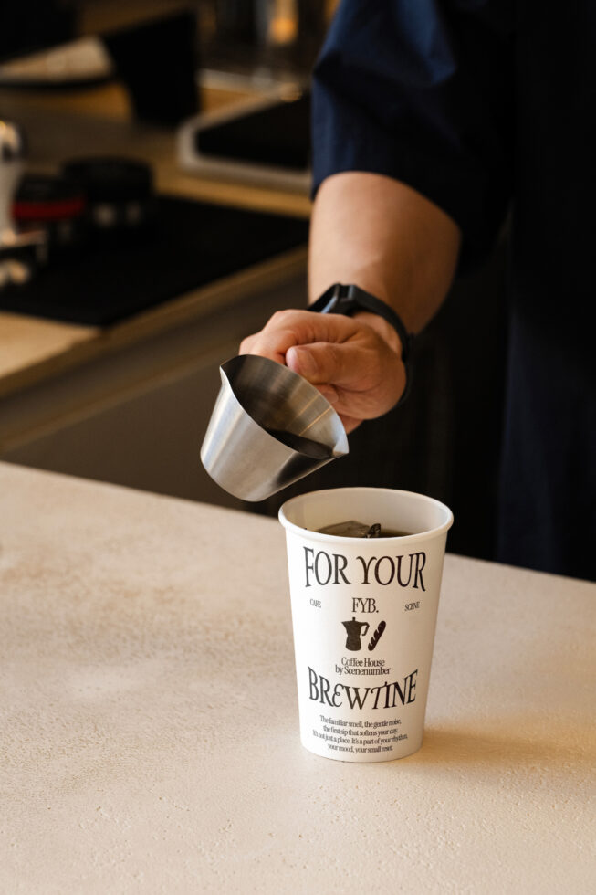 Overhead shot of milk pitcher pouring into branded takeaway cup