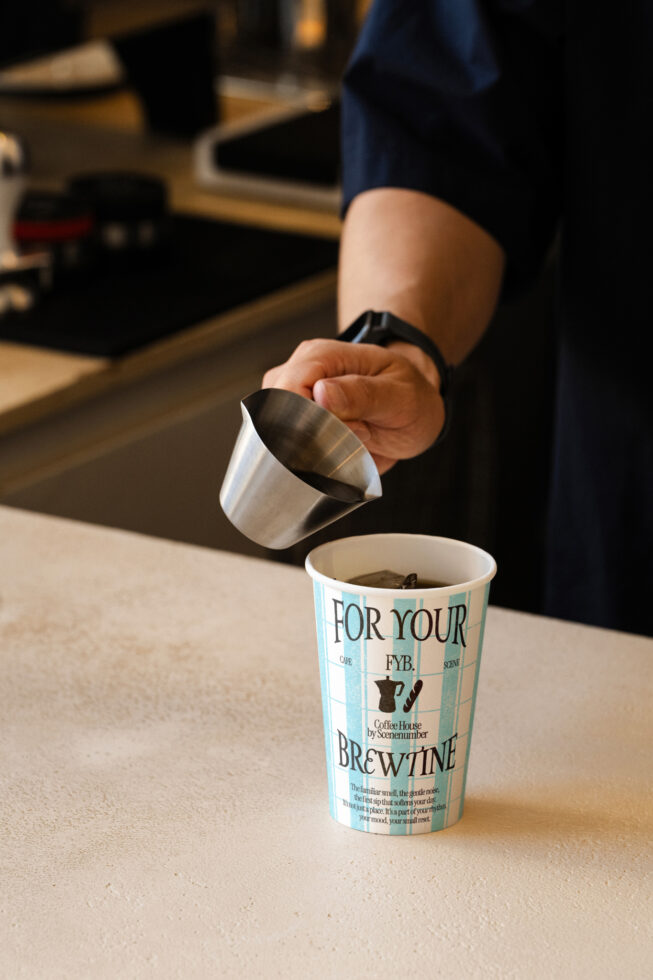 Milk steaming pitcher pouring into paper coffee cup with minimalist branding
