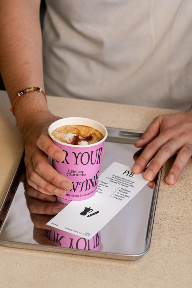 Hands holding pink coffee cup with latte over tray, white menu beside beverage
