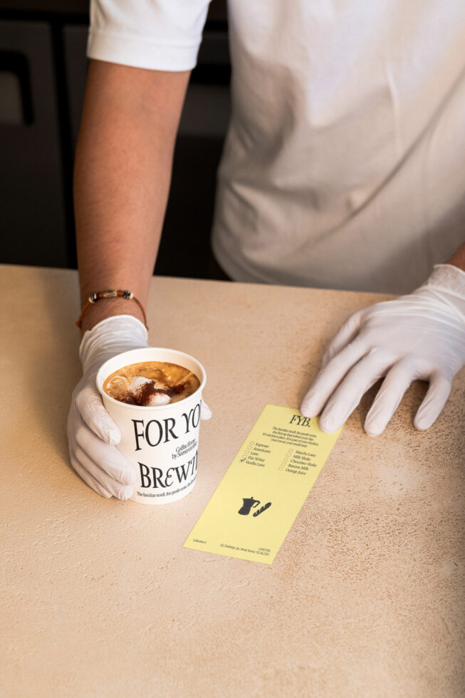 Hands holding white coffee cup with latte, yellow menu card on beige table