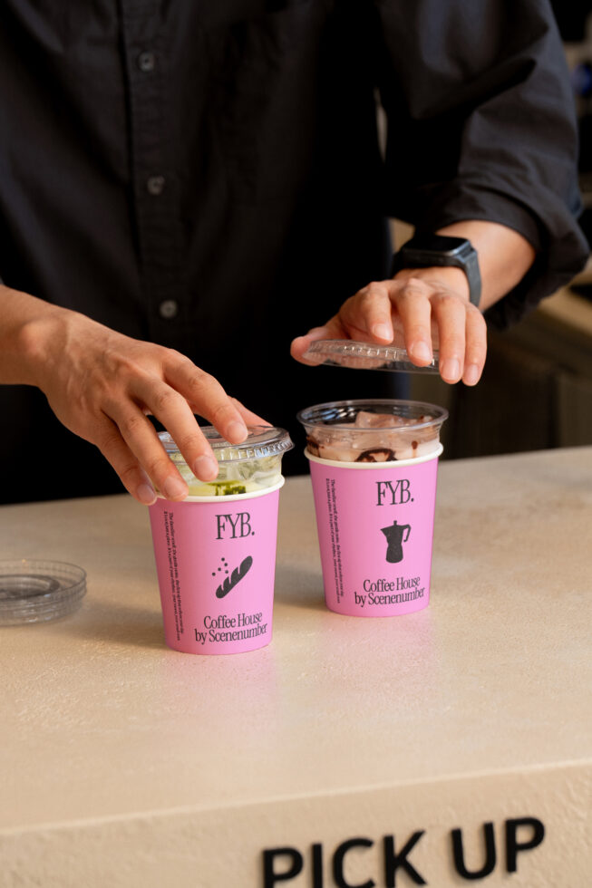 Person holding two pink FYB coffee cups with drinks on pickup counter