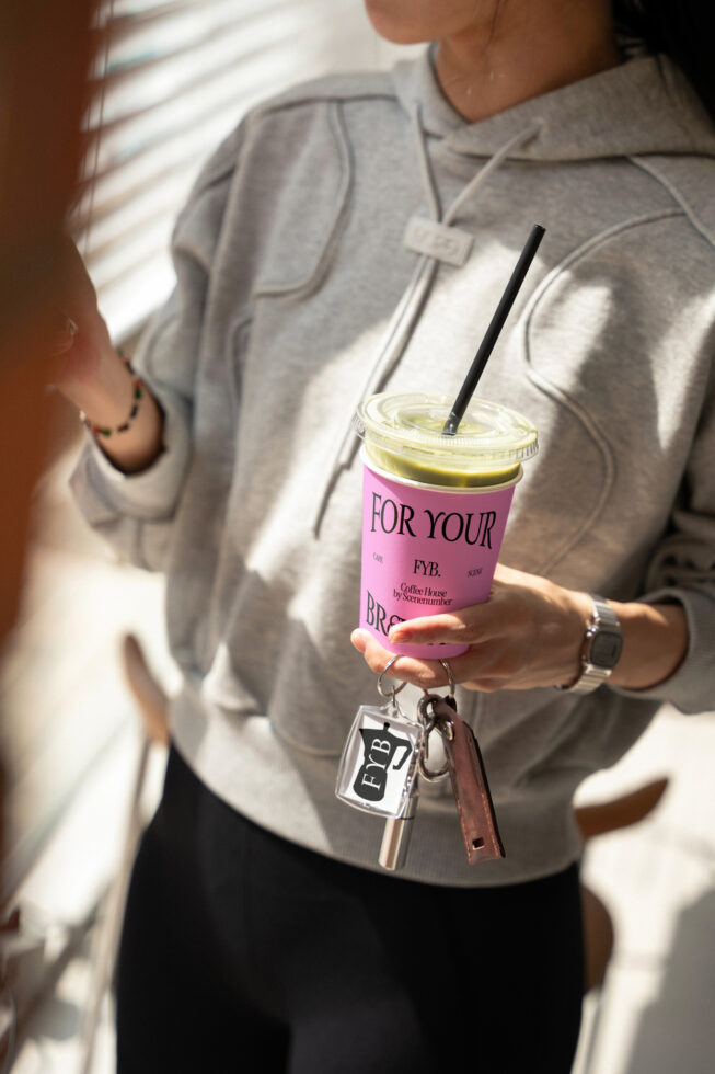 Person in denim holding pink branded cup with iced matcha drink with branded keychain