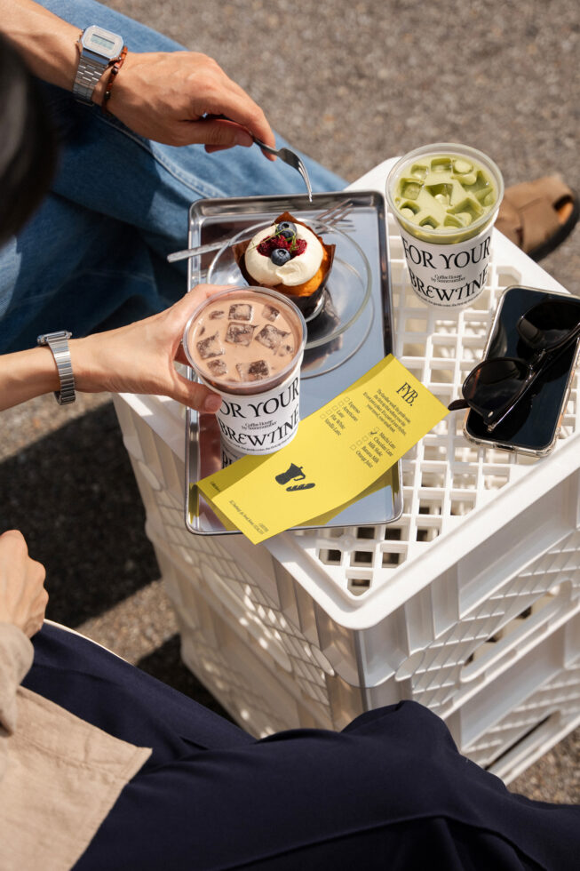 Overhead shot of two iced drinks, pastry, receipt, phone on white tray outdoors
