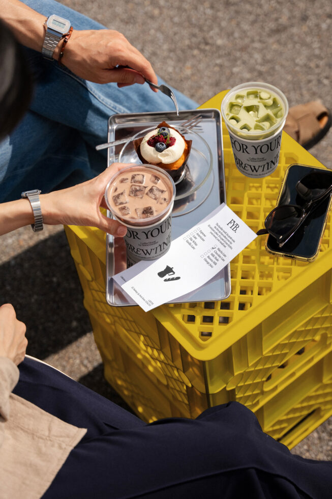 Overhead shot of coffee drinks, pastry on tray, receipt, sunglasses in bright plastic crate