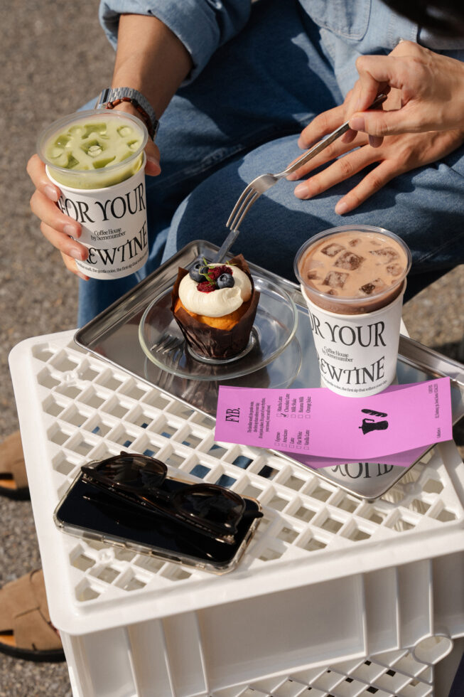 Person holding green matcha drink with chocolate dessert, brown coffee cup on tray