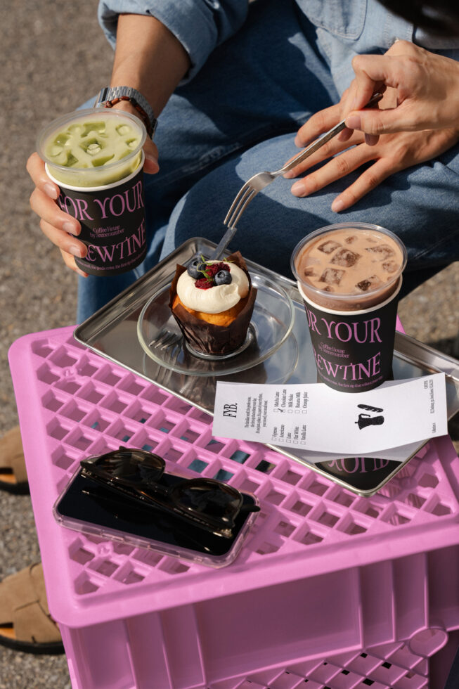 Close-up of two iced coffee cups, chocolate pastry with berries on tray, pink plastic crate setup