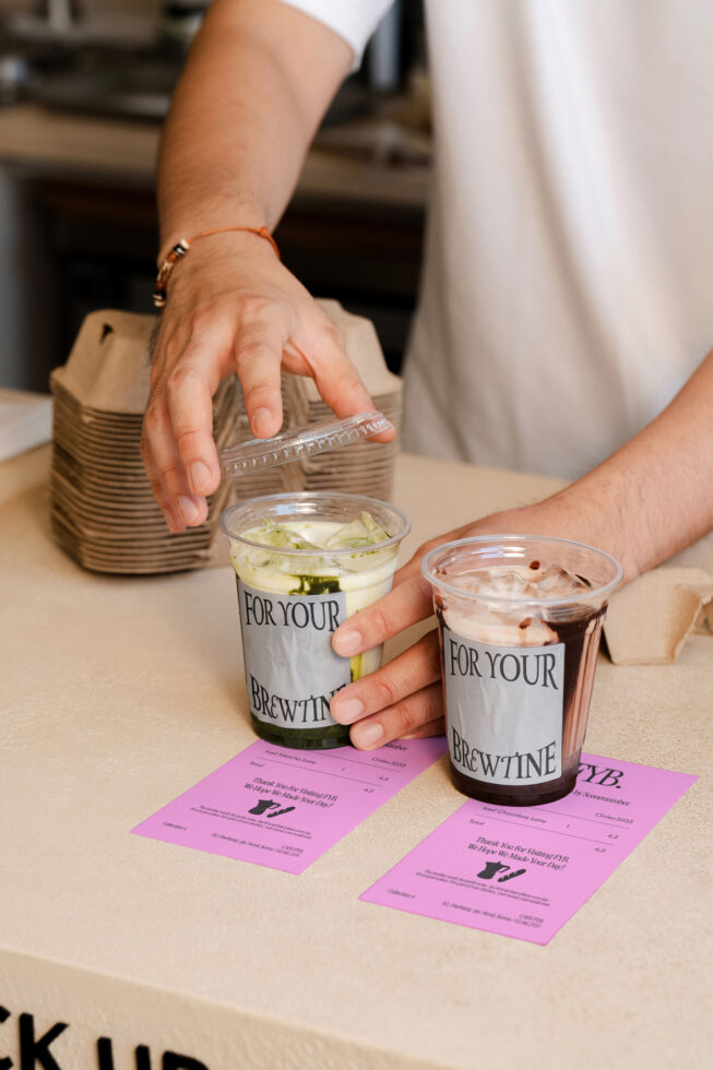 Coffee cup sleeve mockup with pink label held by hand over drinks