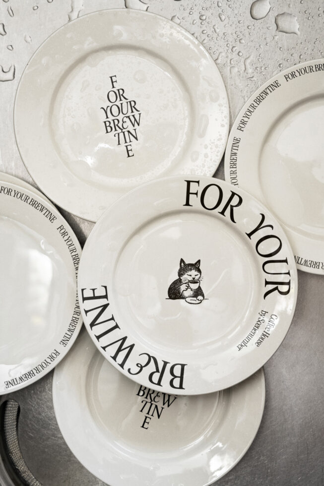 Cream white ceramic plates stacked with cat illustration, brewtine text wrapping rim