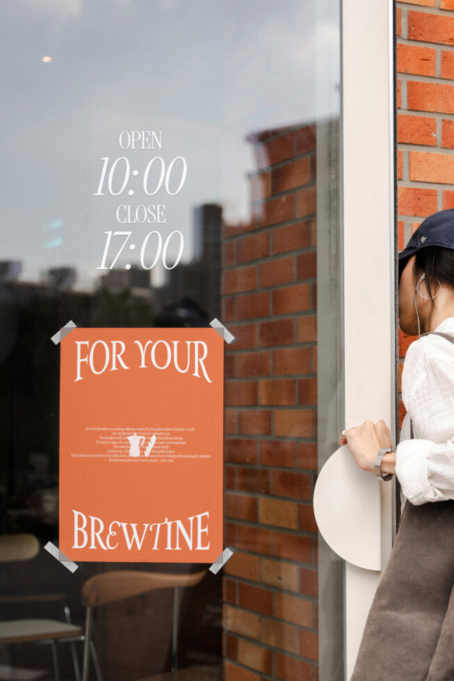 Orange cafe poster on glass door showing hours, brewtine branding taped corners