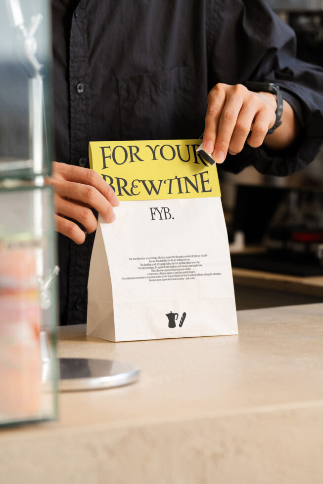 Hands holding white paper bag with yellow banner For Your Brewtine branding