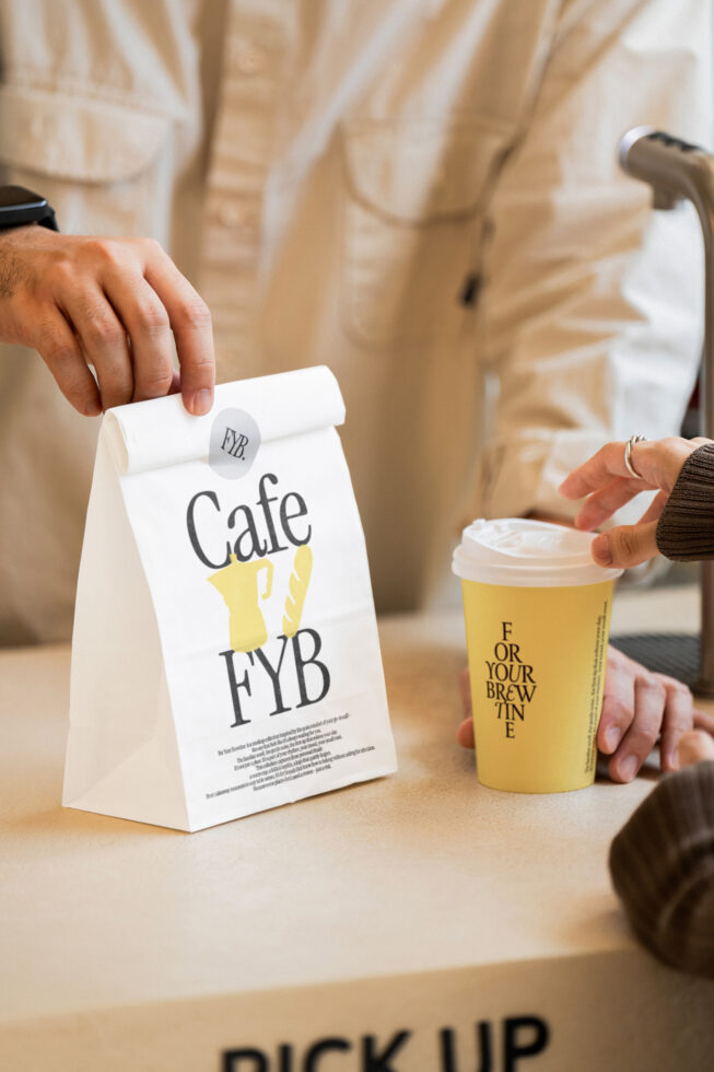 White paper bag with cafe branding next to yellow beverage cup on counter