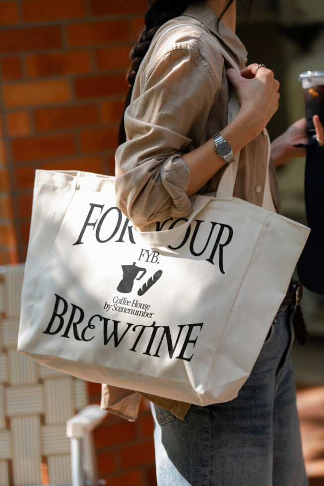 Cream canvas tote bag with For Your Brewtine coffee shop design held by person in beige shirt