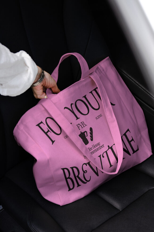Magenta pink tote bag with For Your Brewtine text being held against minimalist dark background