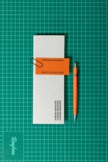 White folder with orange label band, orange pen on teal gridded surface