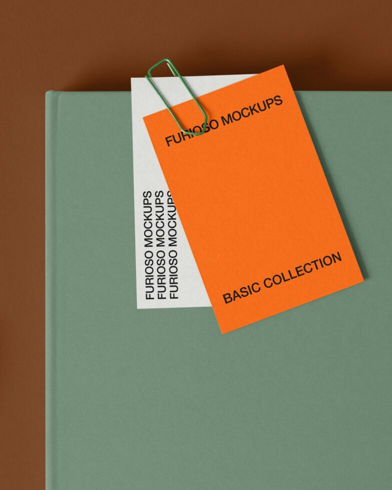 Green book with orange card held by green paperclip on brown backdrop