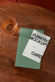 Green notebook mockup layered on wooden table next to drink glass