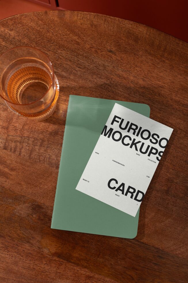 Green notebook mockup layered on wooden table next to drink glass