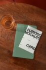 Green notebook mockup layered on wooden table next to drink glass