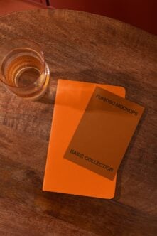 Bright orange notebook mockup on wooden table with amber glass nearby