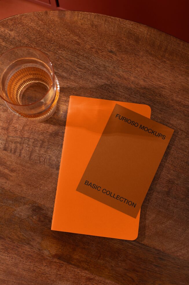 Bright orange notebook mockup on wooden table with amber glass nearby