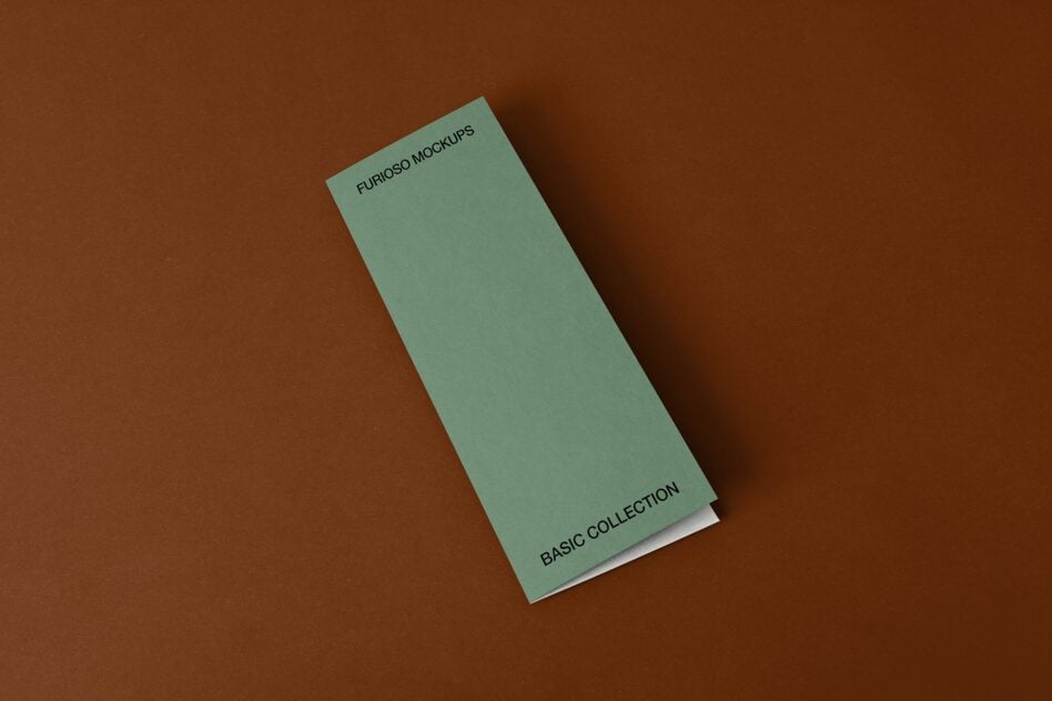 Tall sage green folded brochure with small text on cream base against brown backdrop