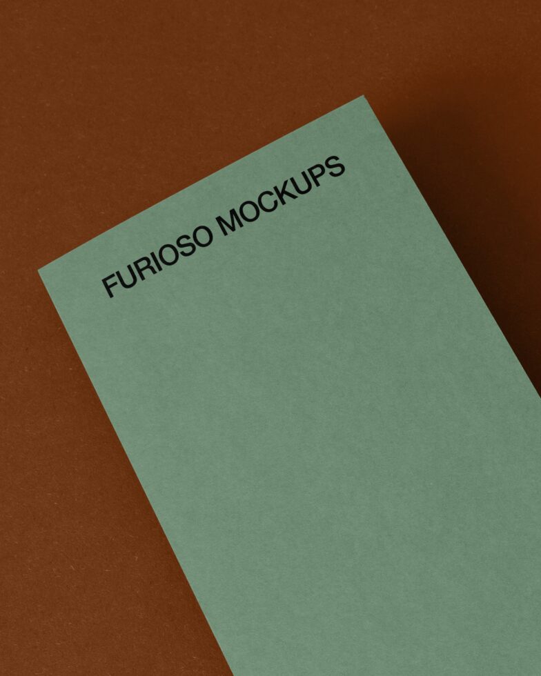 Sage green square card tilted at angle showing small black text on brown surface