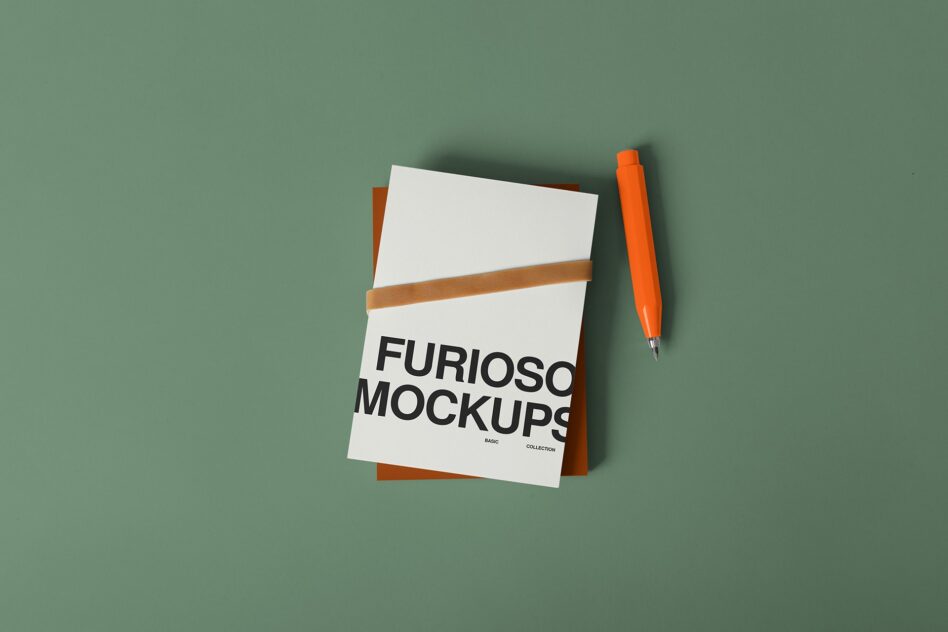 White notepad with tan band, orange pen on green background, papers layered