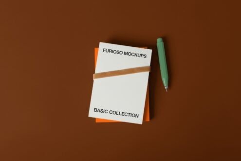 Notepad with tan band, green pen, stacked orange papers on brown backdrop