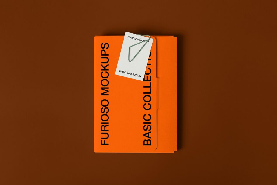 Flat lay of orange box with white card featuring green paperclip on brown surface