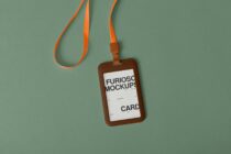 Brown leather ID badge holder with orange lanyard on sage green background
