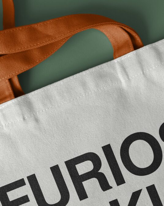 Detail shot of rust handles on natural canvas bag against green background