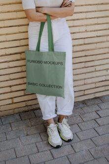 Green tote bag with black text worn over shoulder by person in white pants