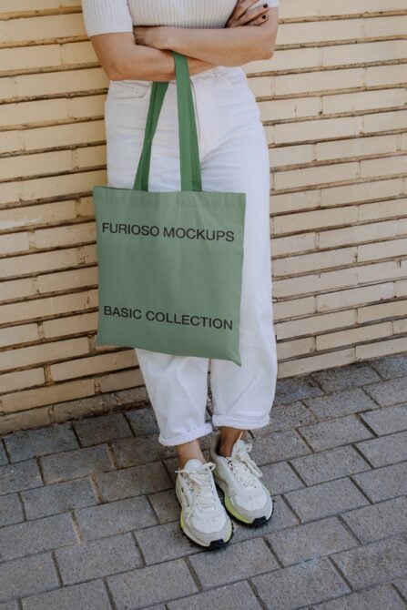 Green tote bag with black text worn over shoulder by person in white pants