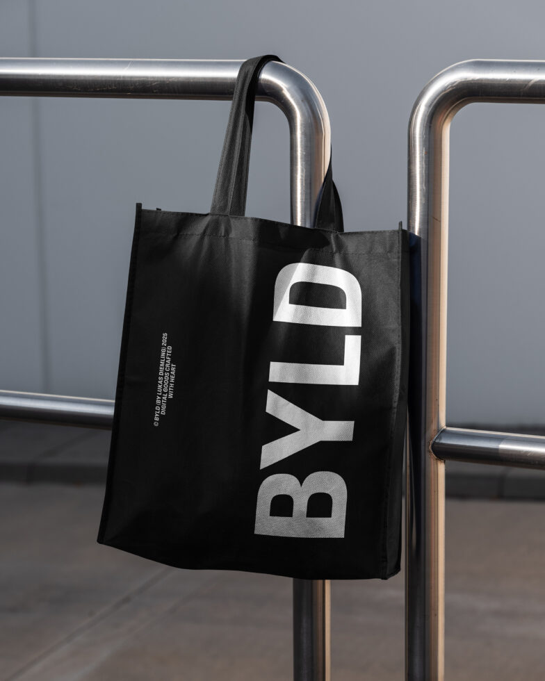 Black tote bag with large silver BYLD lettering hanging on metal rail
