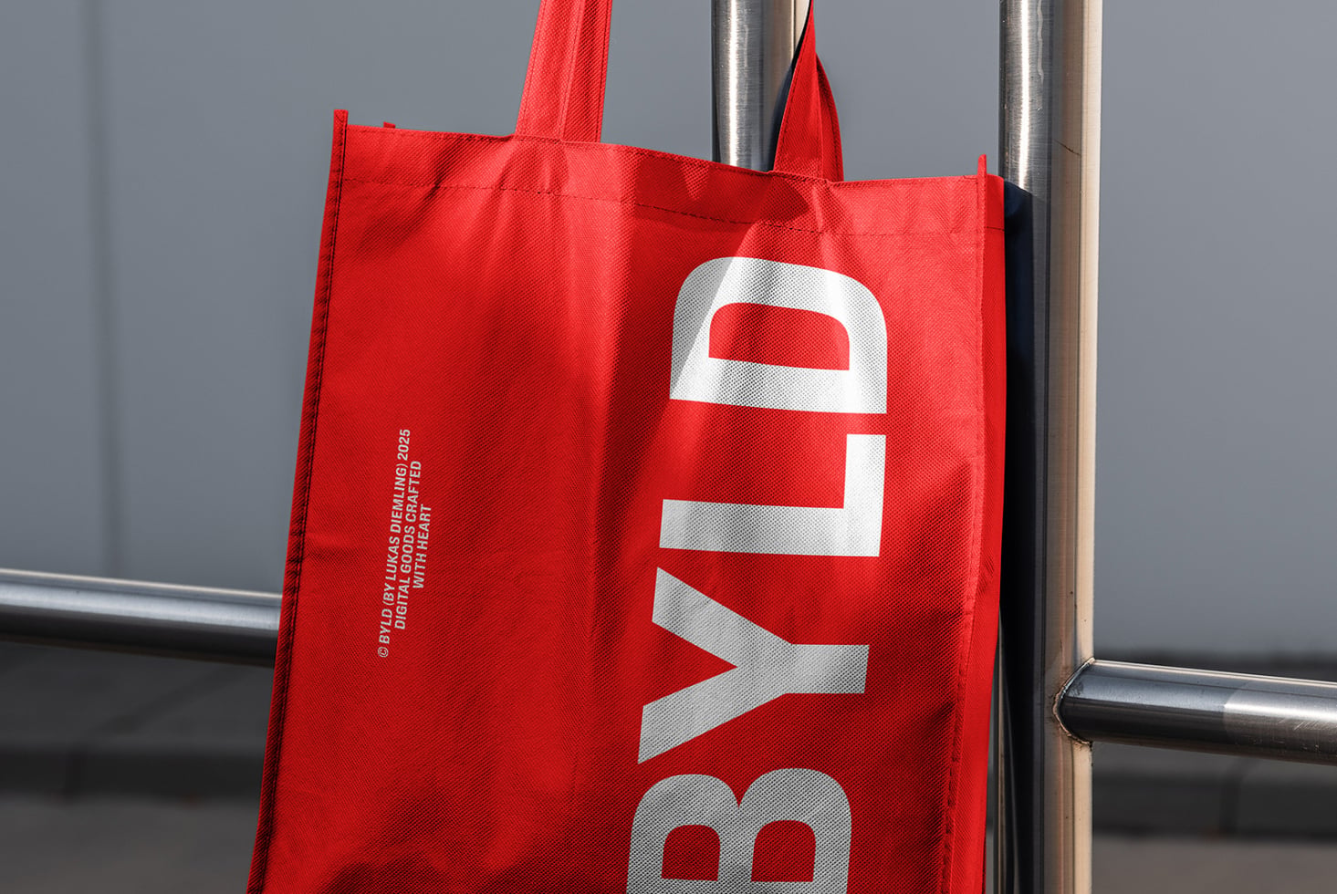Red tote bag with white BYLD text displayed on industrial pipe