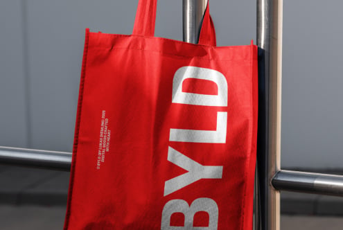 Red tote bag with white BYLD text displayed on industrial pipe
