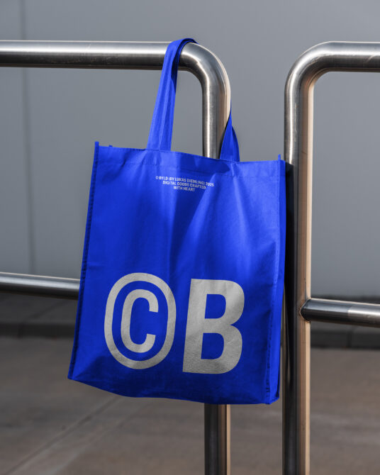 Bright blue tote with silver outlined CB letters on metal railing