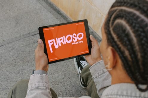 Person holding tablet with orange screen displaying Furioso Mockups branding