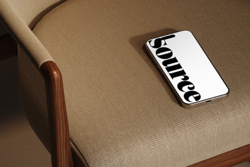 Smartphone resting on beige fabric armchair with wood frame detail