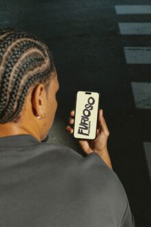 Person holding iPhone displaying Furioso Mockups on cream background