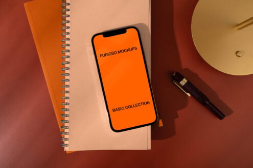Orange phone screen placed on notepad next to pen, lamp, colorful desk setup