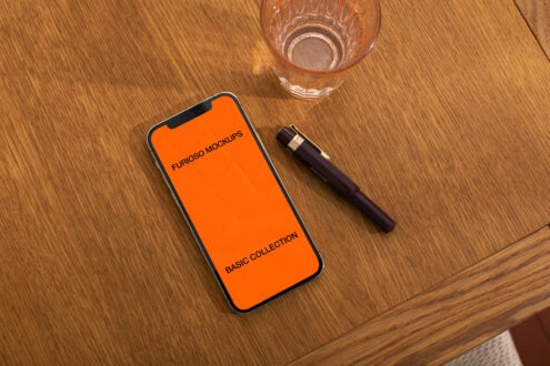 Bright orange iPhone mockup on wood surface with glass water cup nearby