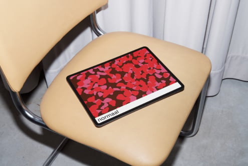 Tablet on beige chair displaying red heart pattern with Normaal branding